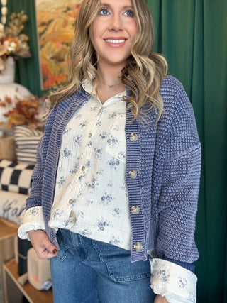 Woman wearing a denim-blue and ivory marled knit button-front cardigan with oversized buttons and dropped shoulders.