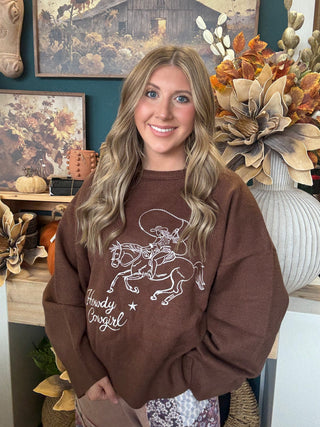 Woman wearing a chocolate-brown Howdy Cowgirl sweater with cream embroidered cowgirl and horse graphic