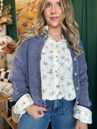 Woman wearing a denim-blue and ivory marled knit button-front cardigan with oversized buttons and dropped shoulders.