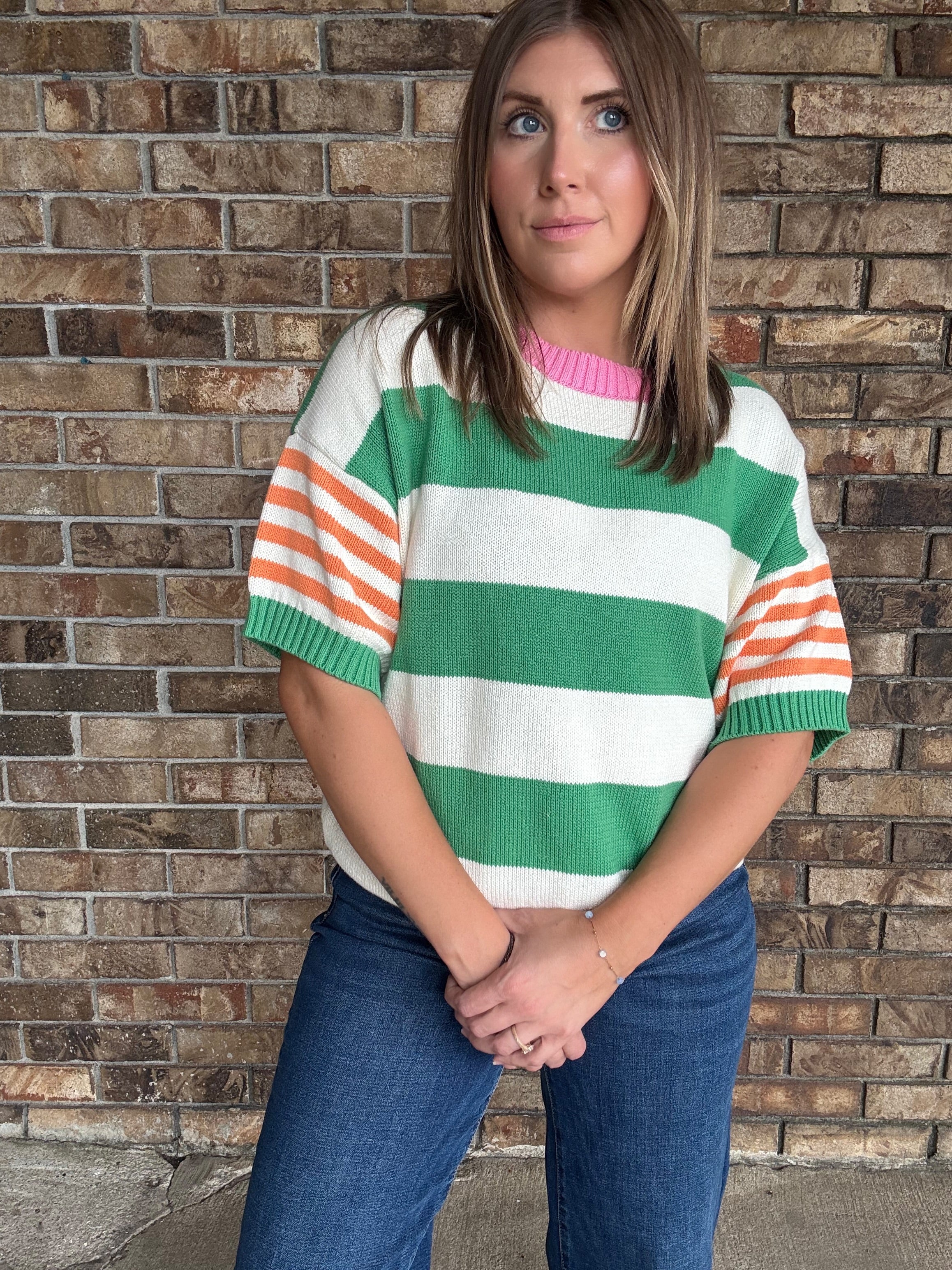 Woman wearing a green and ivory striped lightweight sweater with orange striped sleeves and pink neckline