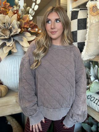 Woman wearing a washed-mocha quilted crew-neck pullover with diamond stitching and exposed seam details