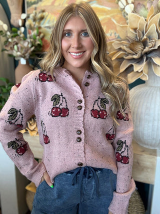 Woman wearing a dusty-pink cherry motif button-front cardigan from Pill Box Boutique
