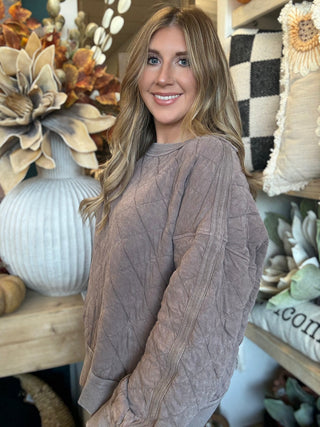 Woman wearing a washed-mocha quilted crew-neck pullover with diamond stitching and exposed seam details