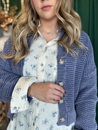 Woman wearing a denim-blue and ivory marled knit button-front cardigan with oversized buttons and dropped shoulders.