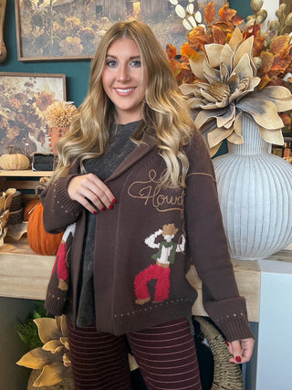 Woman wearing a chocolate-brown open-front cardigan with embroidered “Howdy” script and colorful cowboy motifs