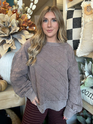 Woman wearing a washed-mocha quilted crew-neck pullover with diamond stitching and exposed seam details