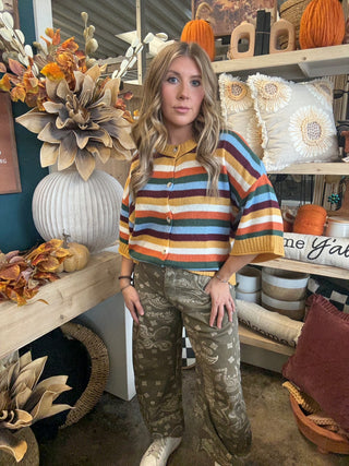 Woman wearing a mustard, cream, rust, forest green, light blue, and burgundy striped button-front sweater.