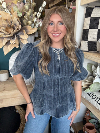 Woman wearing a washed-charcoal peplum top with puff sleeves and pearl bow neckline detail