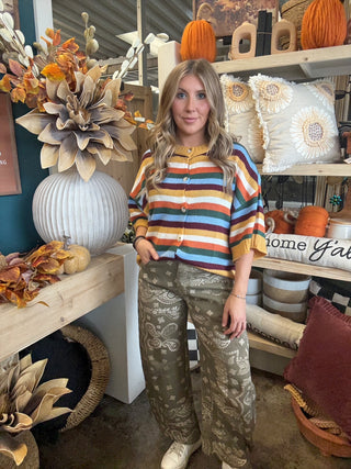 Woman wearing a mustard, cream, rust, forest green, light blue, and burgundy striped button-front sweater.