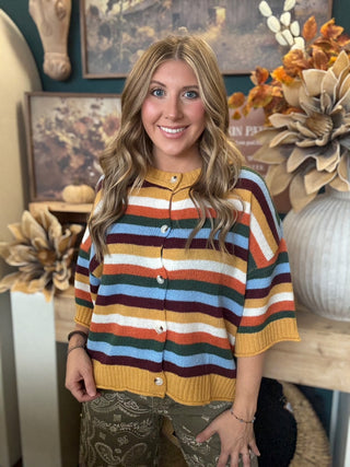 Woman wearing a mustard, cream, rust, forest green, light blue, and burgundy striped button-front sweater.