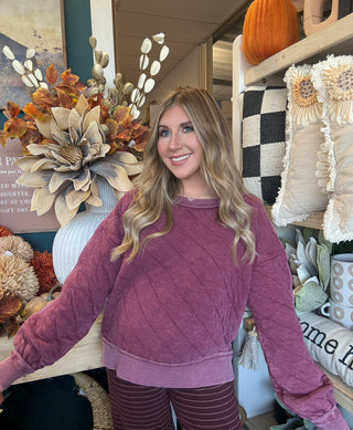 Woman wearing a washed wine quilted crew-neck sweatshirt with diagonal diamond stitching.