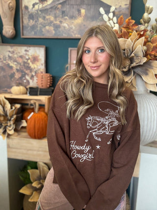 Woman wearing a chocolate-brown Howdy Cowgirl sweater with cream embroidered cowgirl and horse graphic