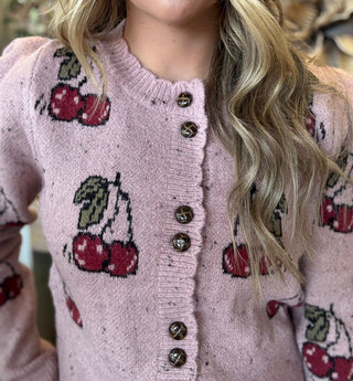 Woman wearing a dusty-pink cherry motif button-front cardigan from Pill Box Boutique