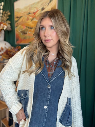 Woman wearing a cream open-knit twofer sweater with a washed-denim button front, flap pockets, and plaid collar accent.