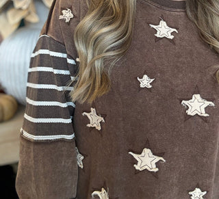 Woman wearing a chocolate vintage-wash pullover with cream appliqué stars and striped sleeves