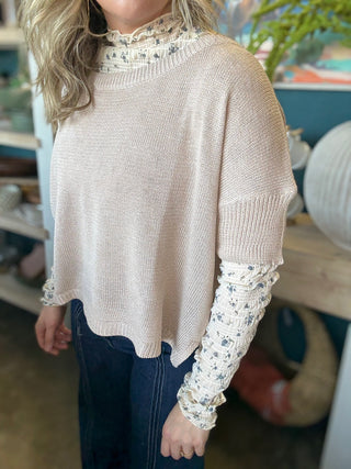 woman wearing oatmeal knit sweater layered over floral textured long sleeve top