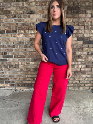 Woman wearing a navy star embroidered ruffle sleeve sweater top with lightweight knit fabric