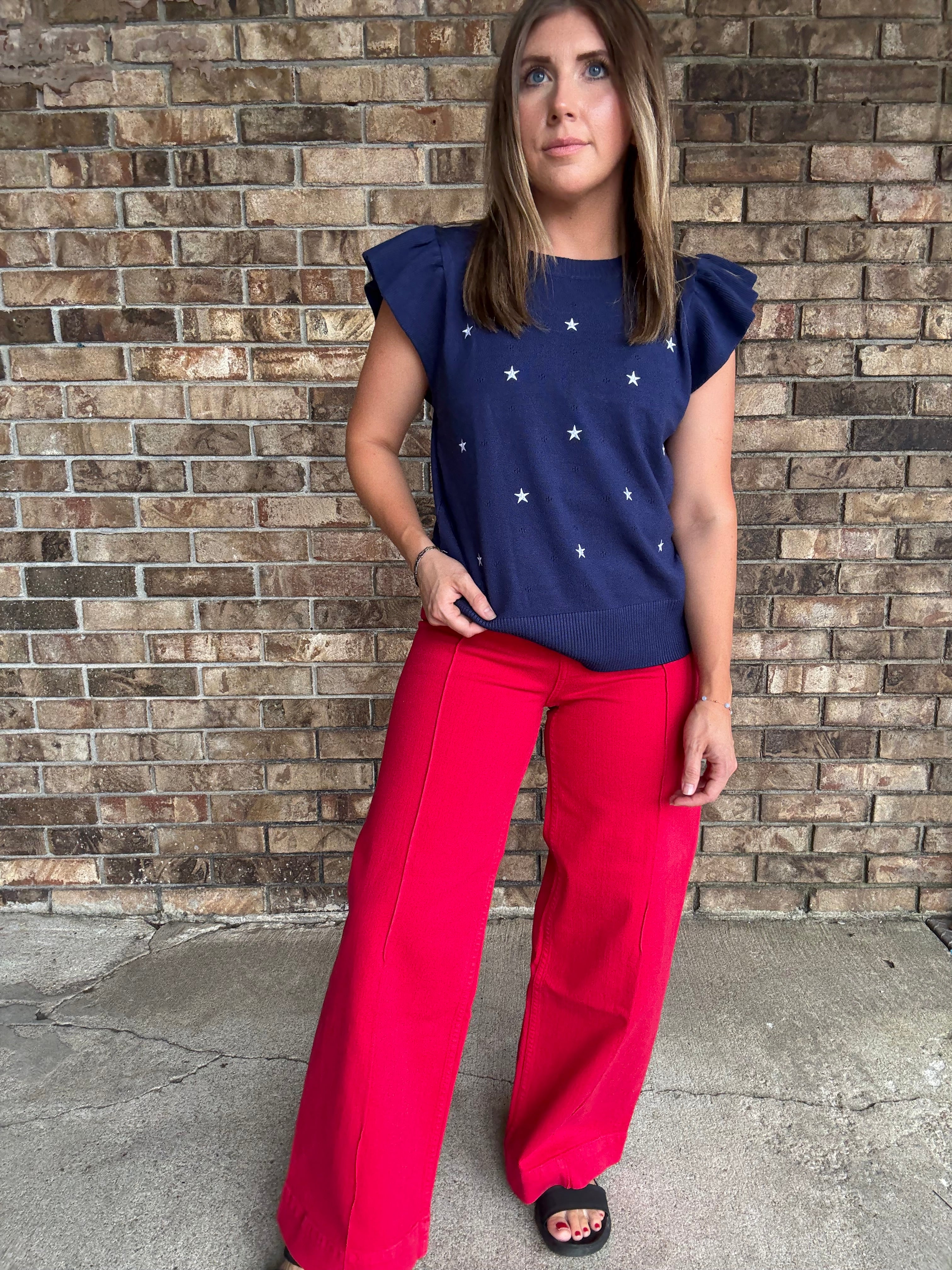 Woman wearing a navy star embroidered ruffle sleeve sweater top with lightweight knit fabric