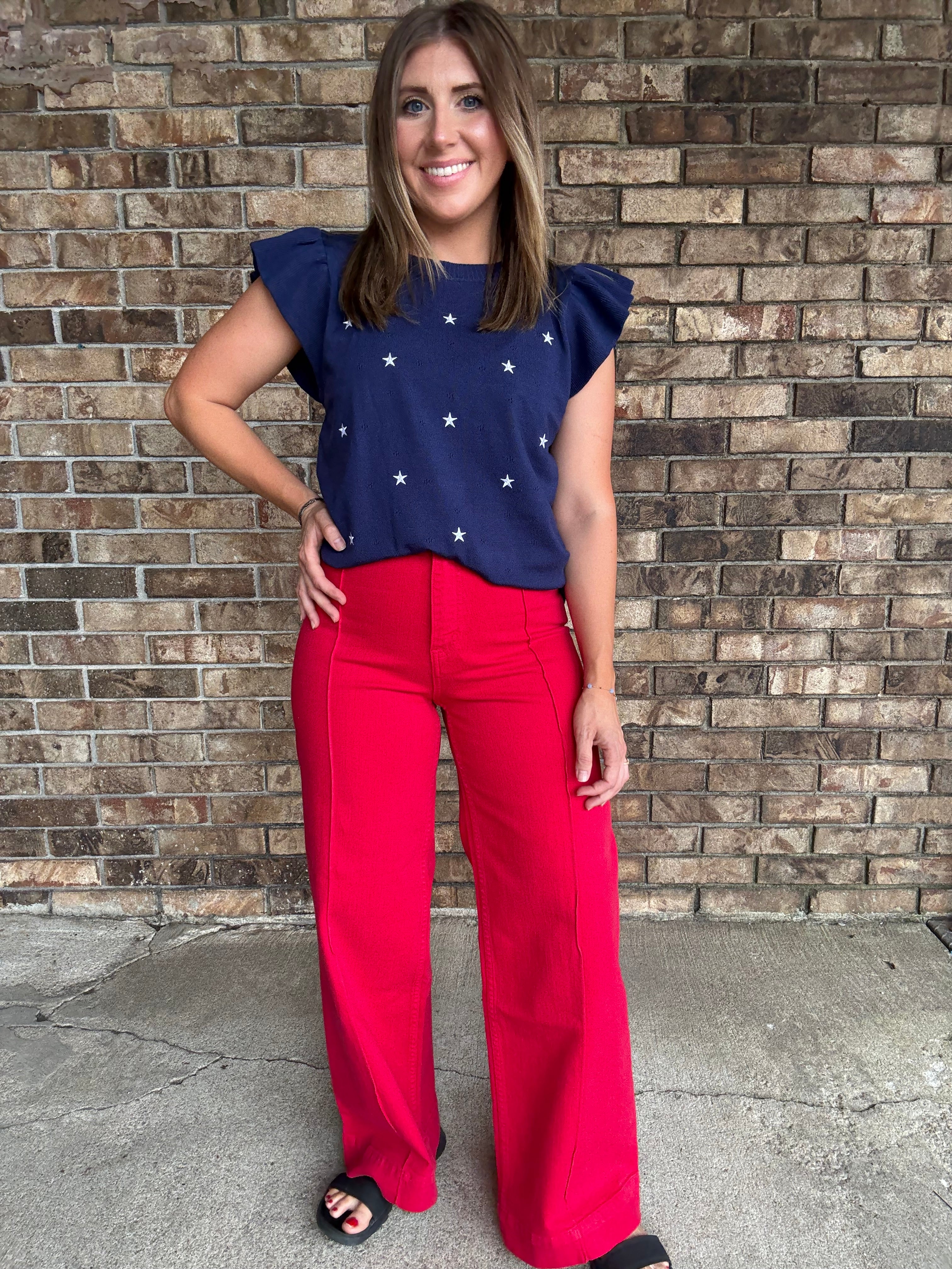 Woman wearing a navy star embroidered ruffle sleeve sweater top with lightweight knit fabric