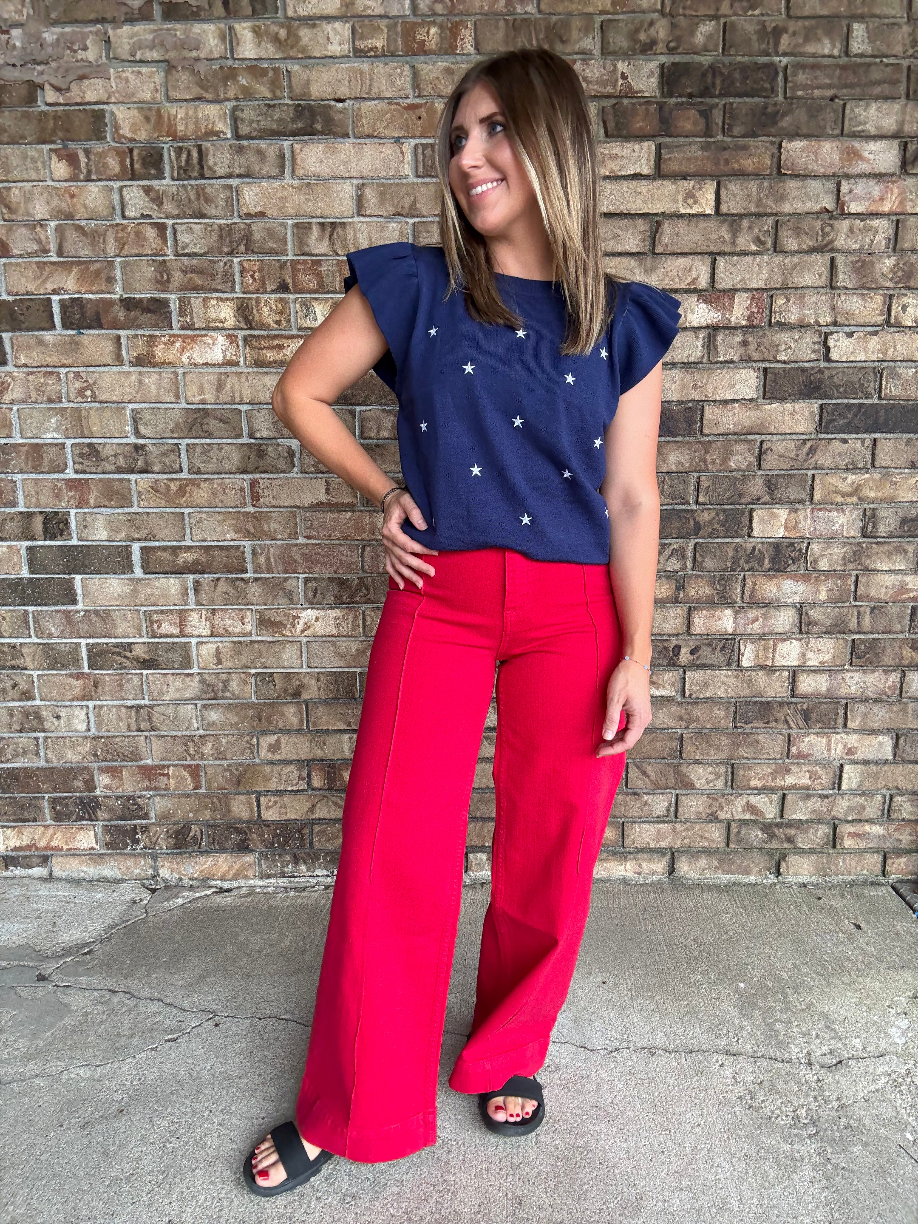 Woman wearing a navy star embroidered ruffle sleeve sweater top with lightweight knit fabric