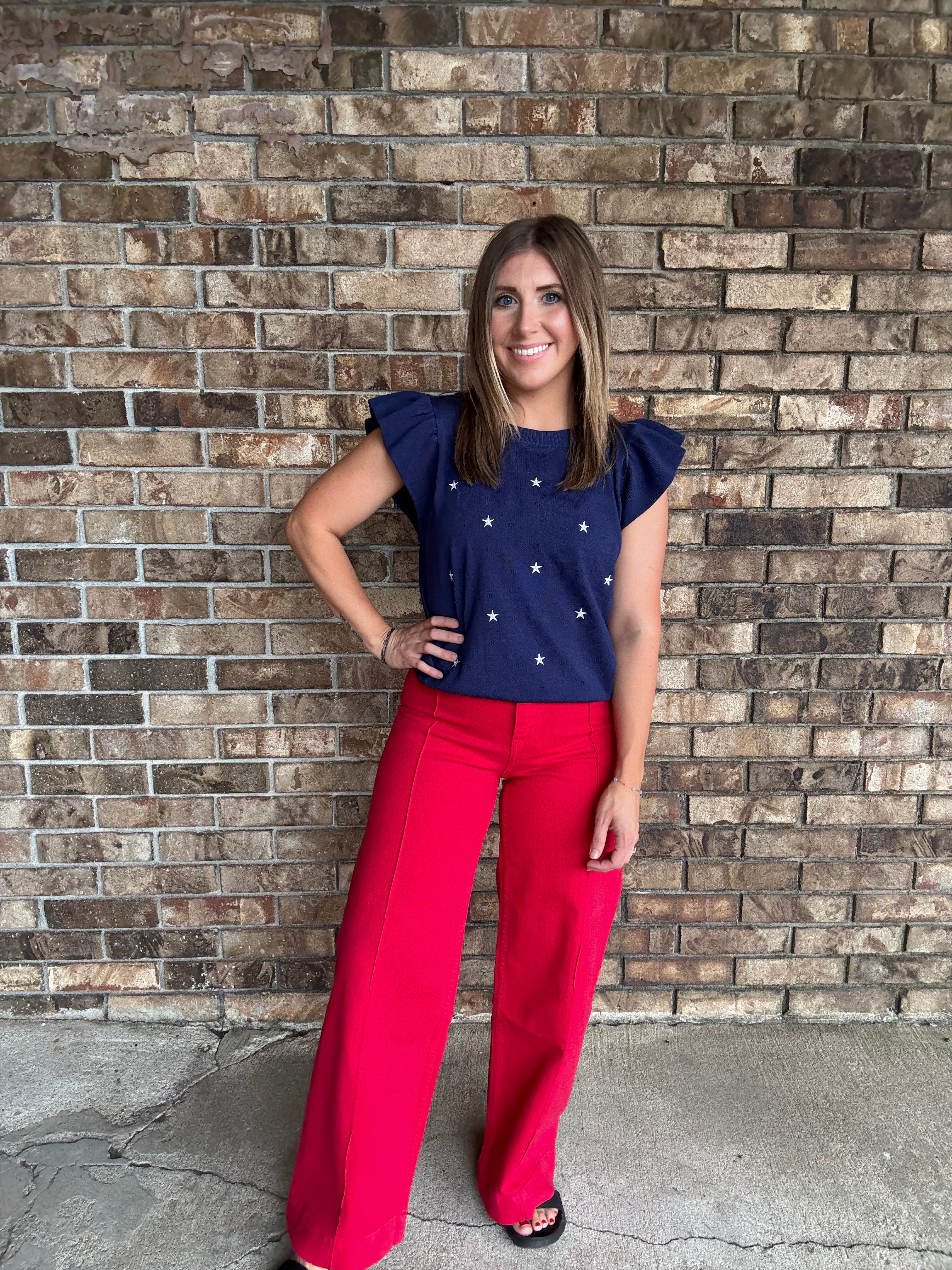 Woman wearing a navy star embroidered ruffle sleeve sweater top with lightweight knit fabric