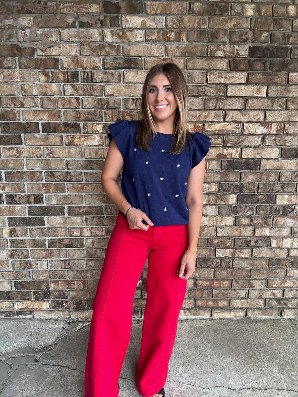 Woman wearing a navy star embroidered ruffle sleeve sweater top with lightweight knit fabric