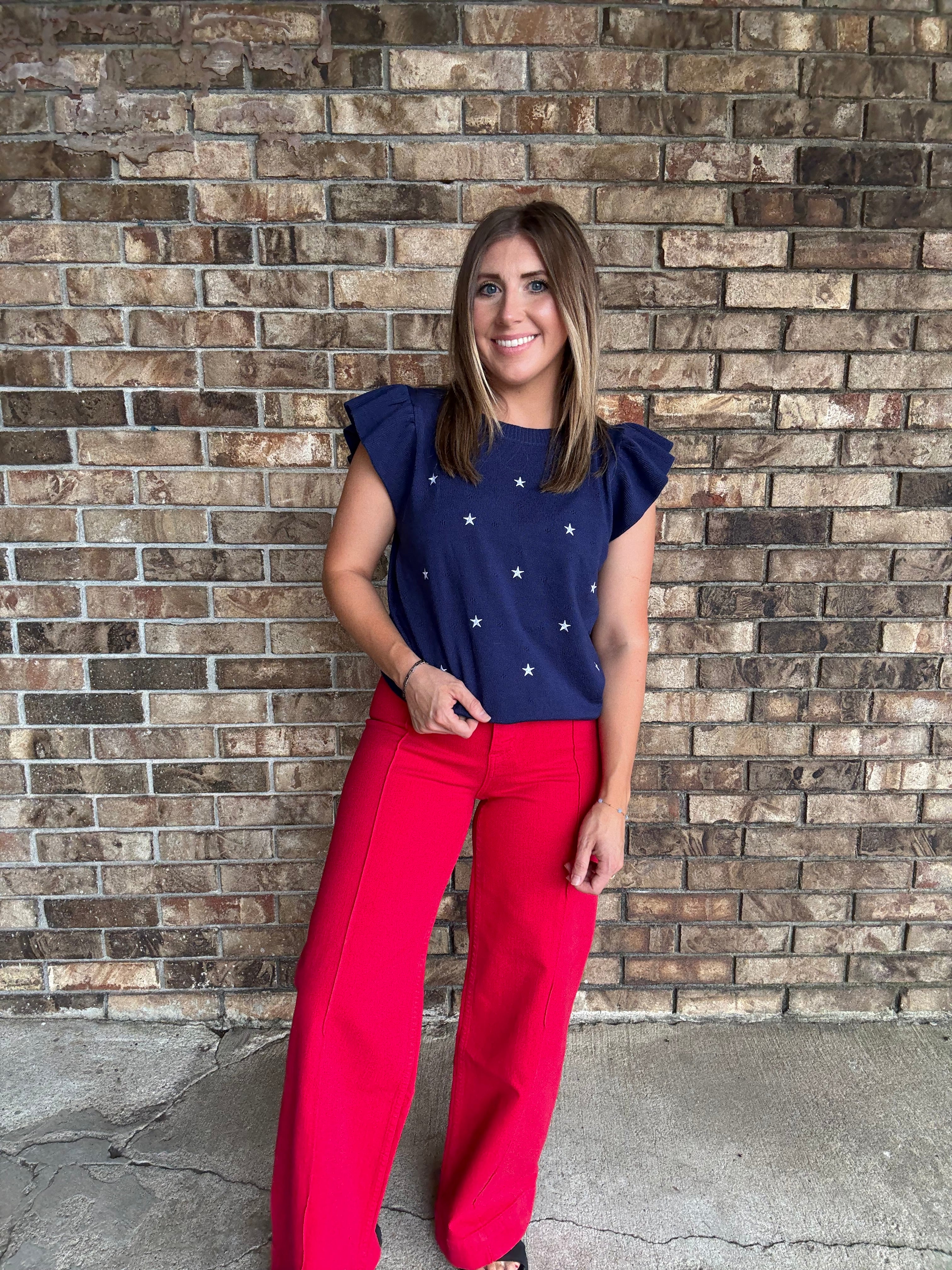 Woman wearing a navy star embroidered ruffle sleeve sweater top with lightweight knit fabric