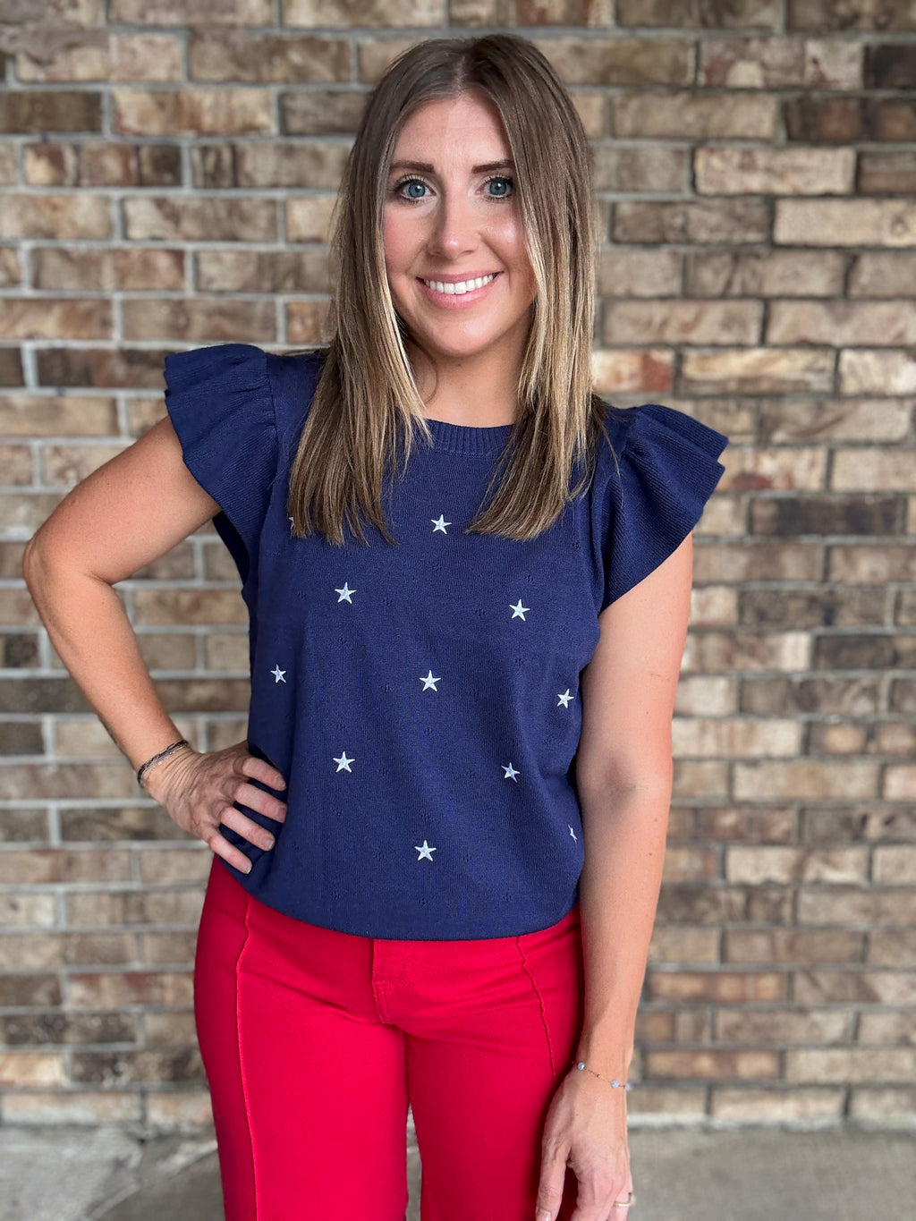 Woman wearing a navy star embroidered ruffle sleeve sweater top with lightweight knit fabric
