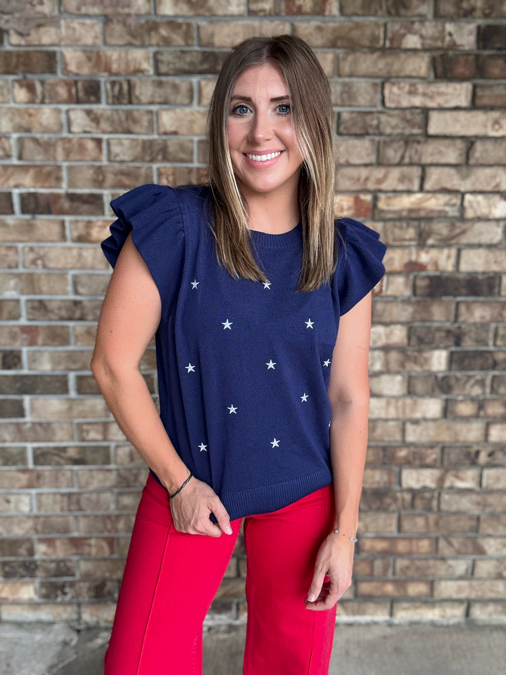 Woman wearing a navy star embroidered ruffle sleeve sweater top with lightweight knit fabric
