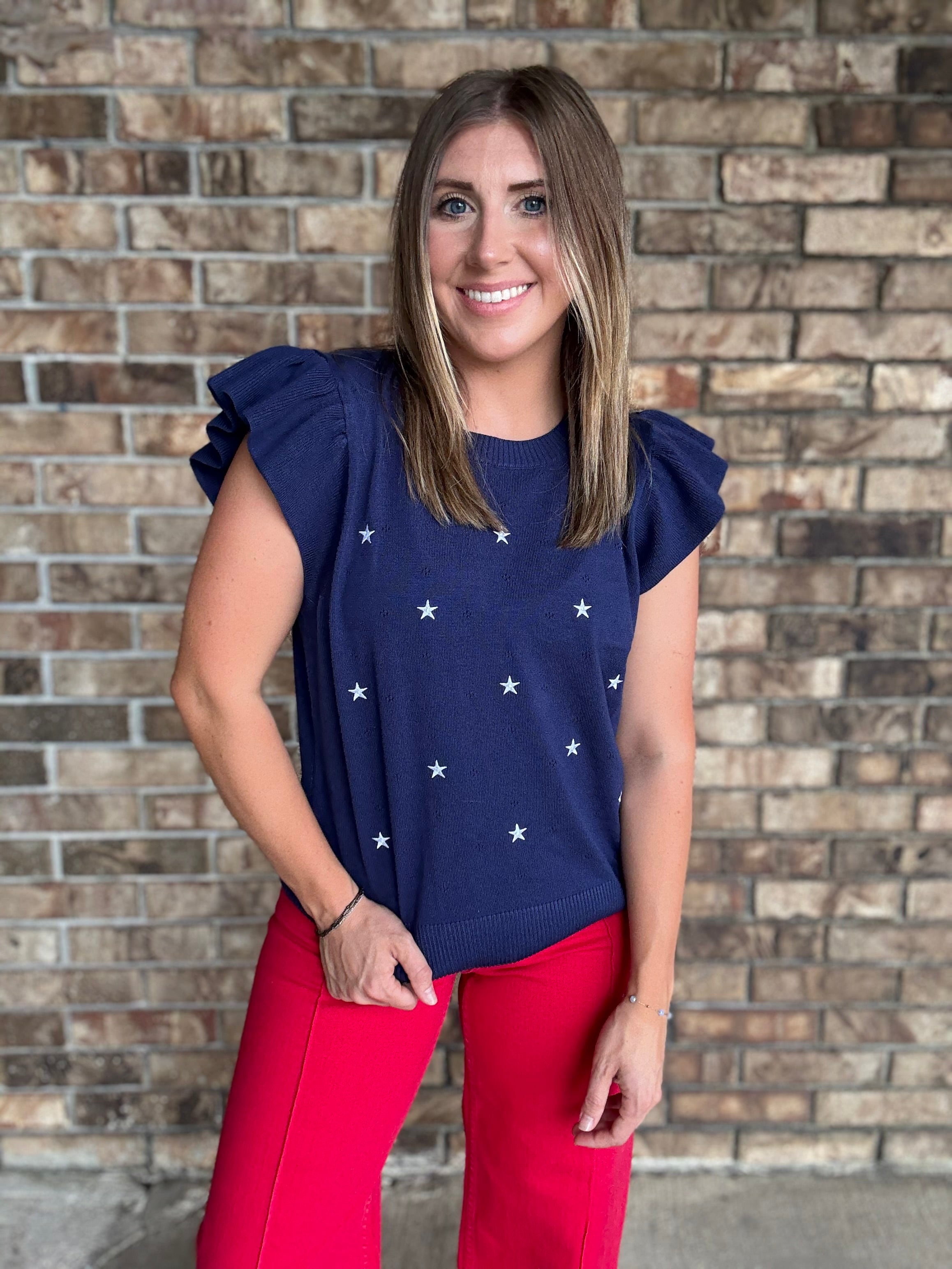 Woman wearing a navy star embroidered ruffle sleeve sweater top with lightweight knit fabric