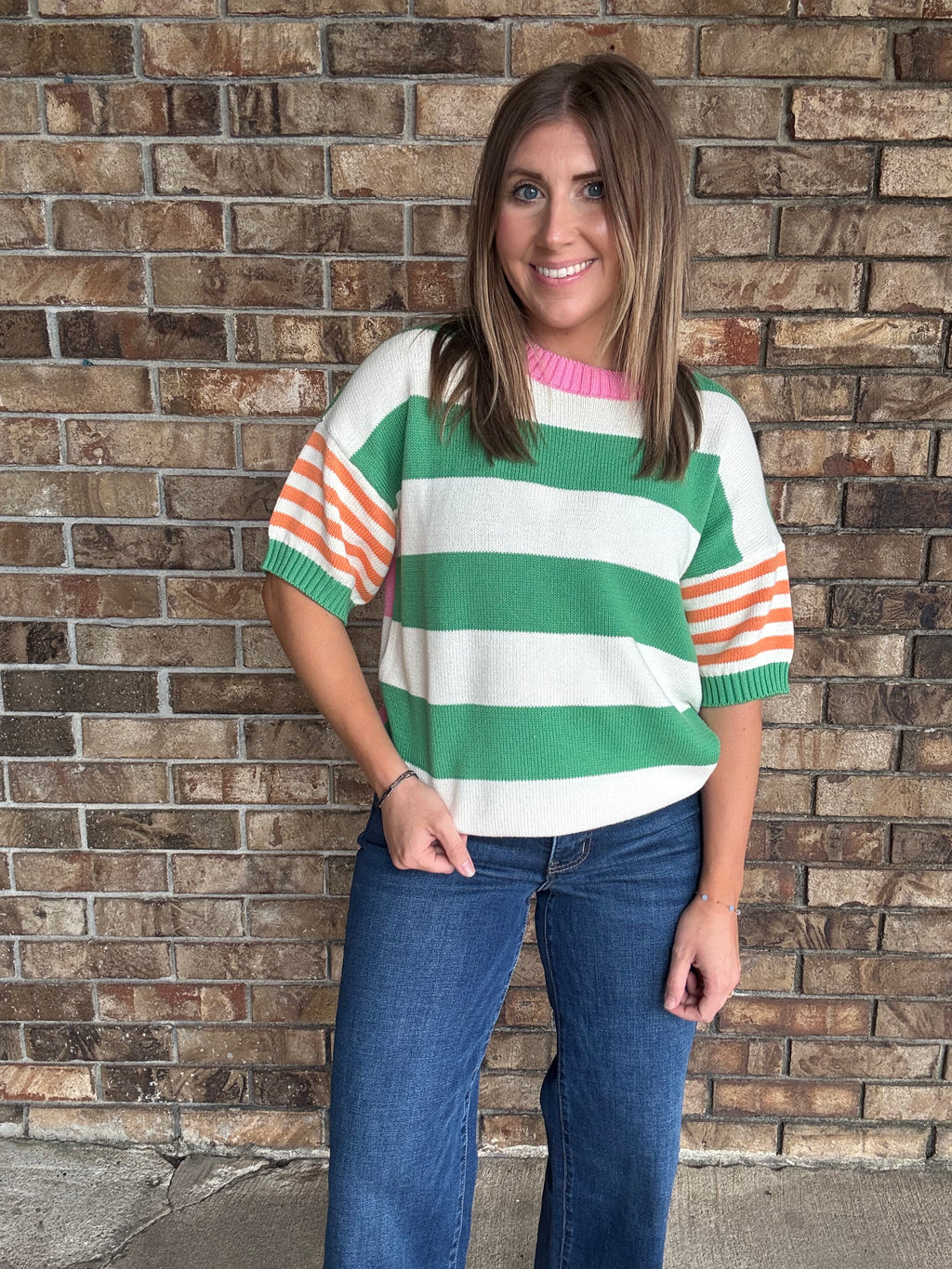 Woman wearing a green and ivory striped lightweight sweater with orange striped sleeves and pink neckline