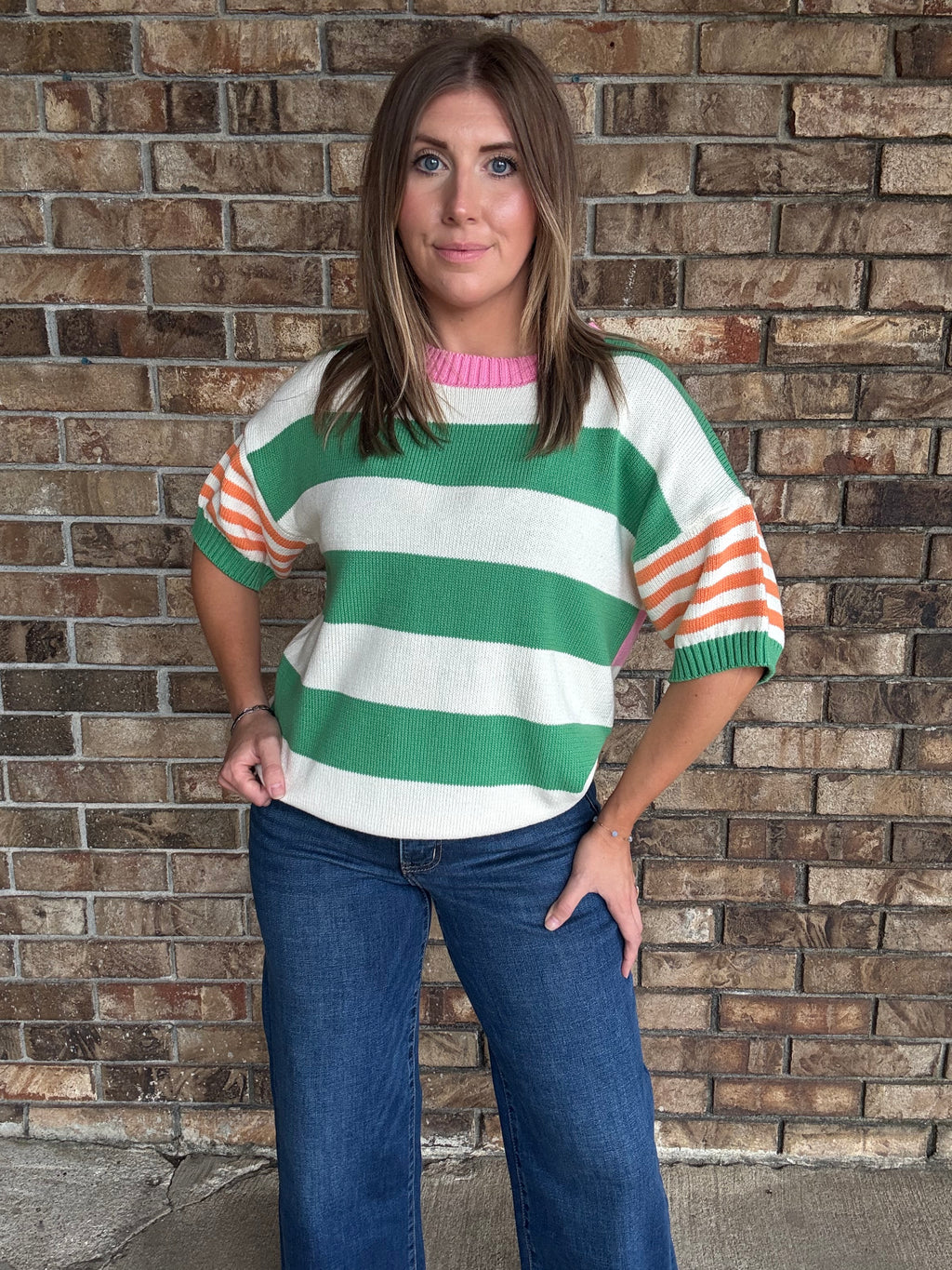 Woman wearing a green and ivory striped lightweight sweater with orange striped sleeves and pink neckline