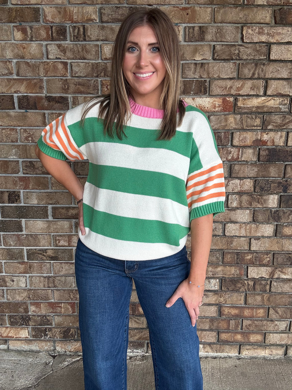 Woman wearing a green and ivory striped lightweight sweater with orange striped sleeves and pink neckline