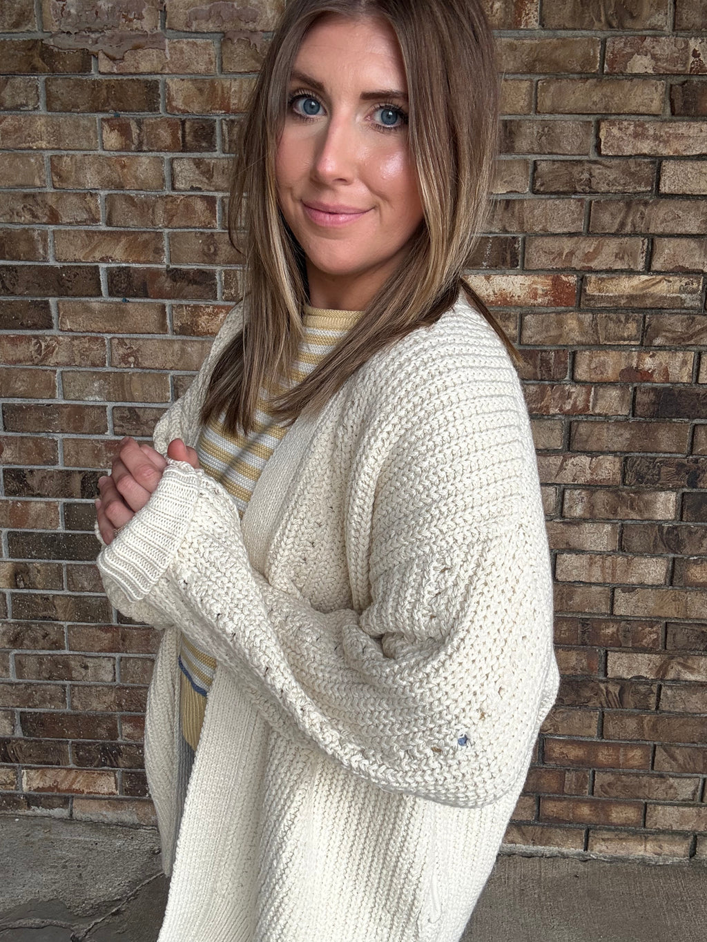 Woman wearing an oversized ivory open knit cardigan layered over a striped sweater and dark wash jeans