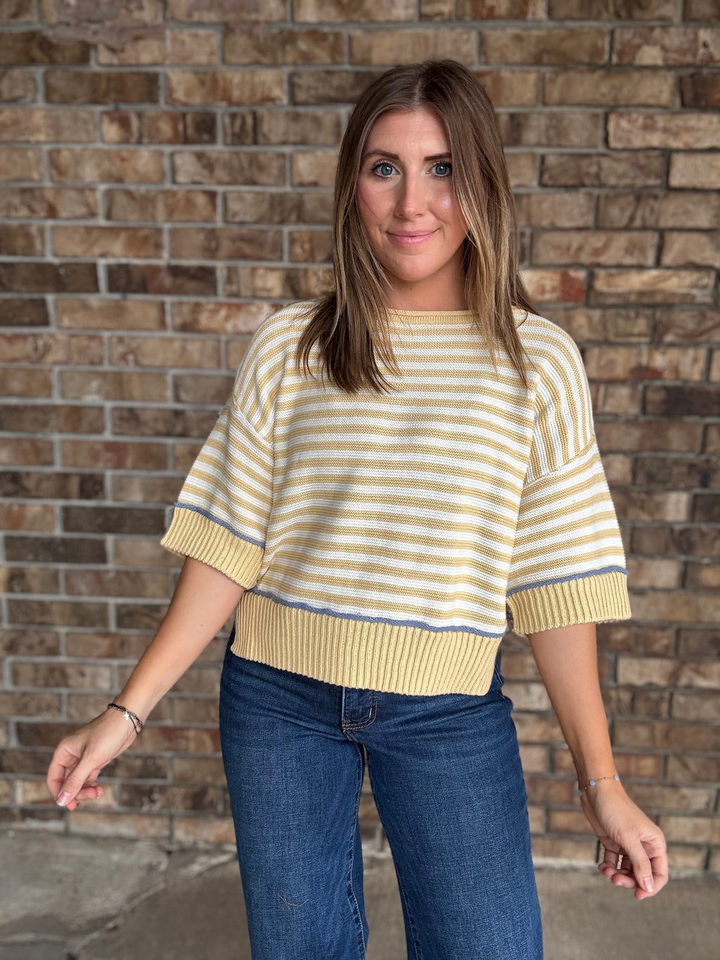 Woman wearing a butter yellow and ivory striped lightweight sweater with raw edge details and dark wash jeans