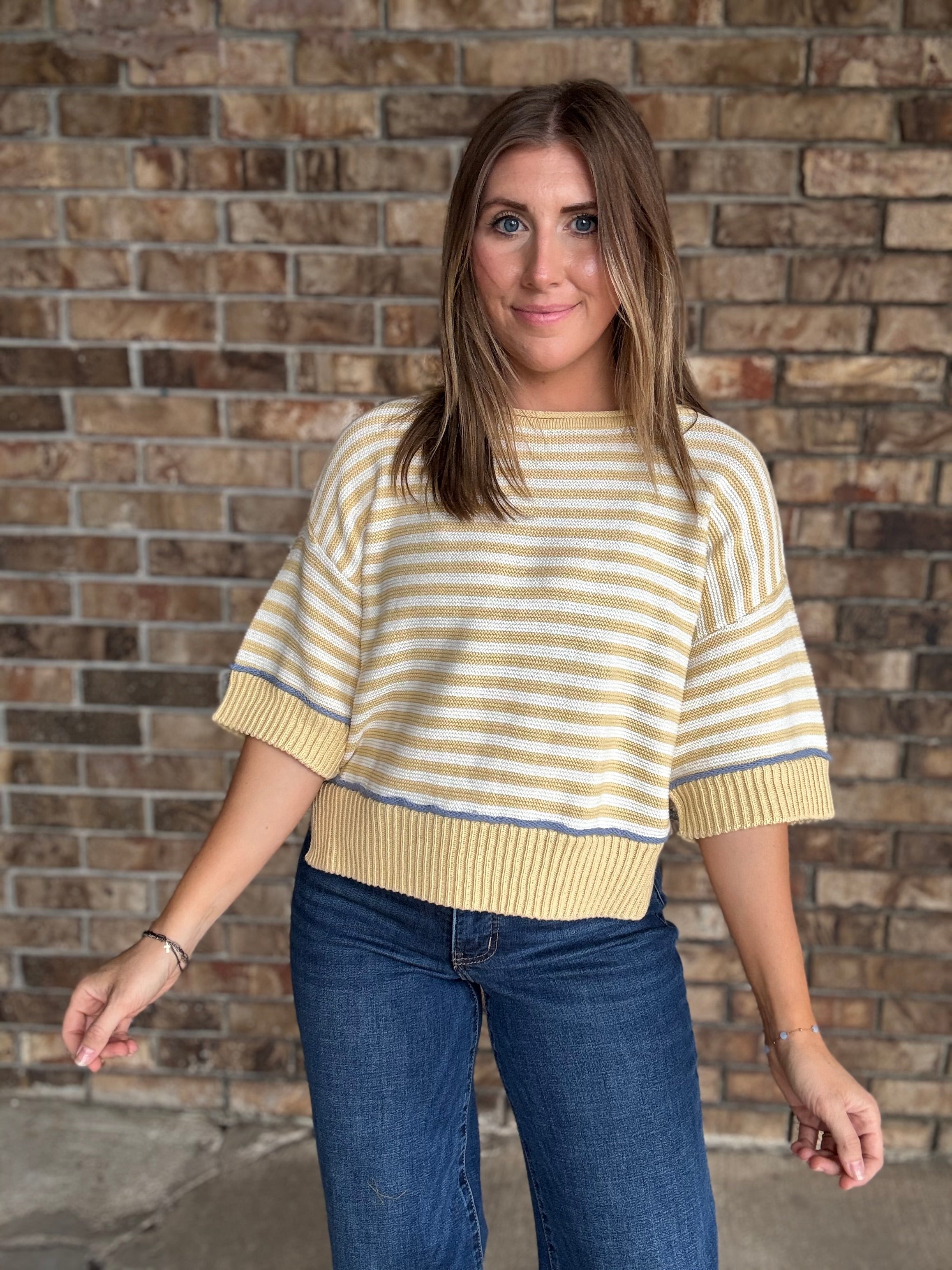 Woman wearing a butter yellow and ivory striped lightweight sweater with raw edge details and dark wash jeans