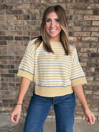 Woman wearing a butter yellow and ivory striped lightweight sweater with raw edge details and dark wash jeans