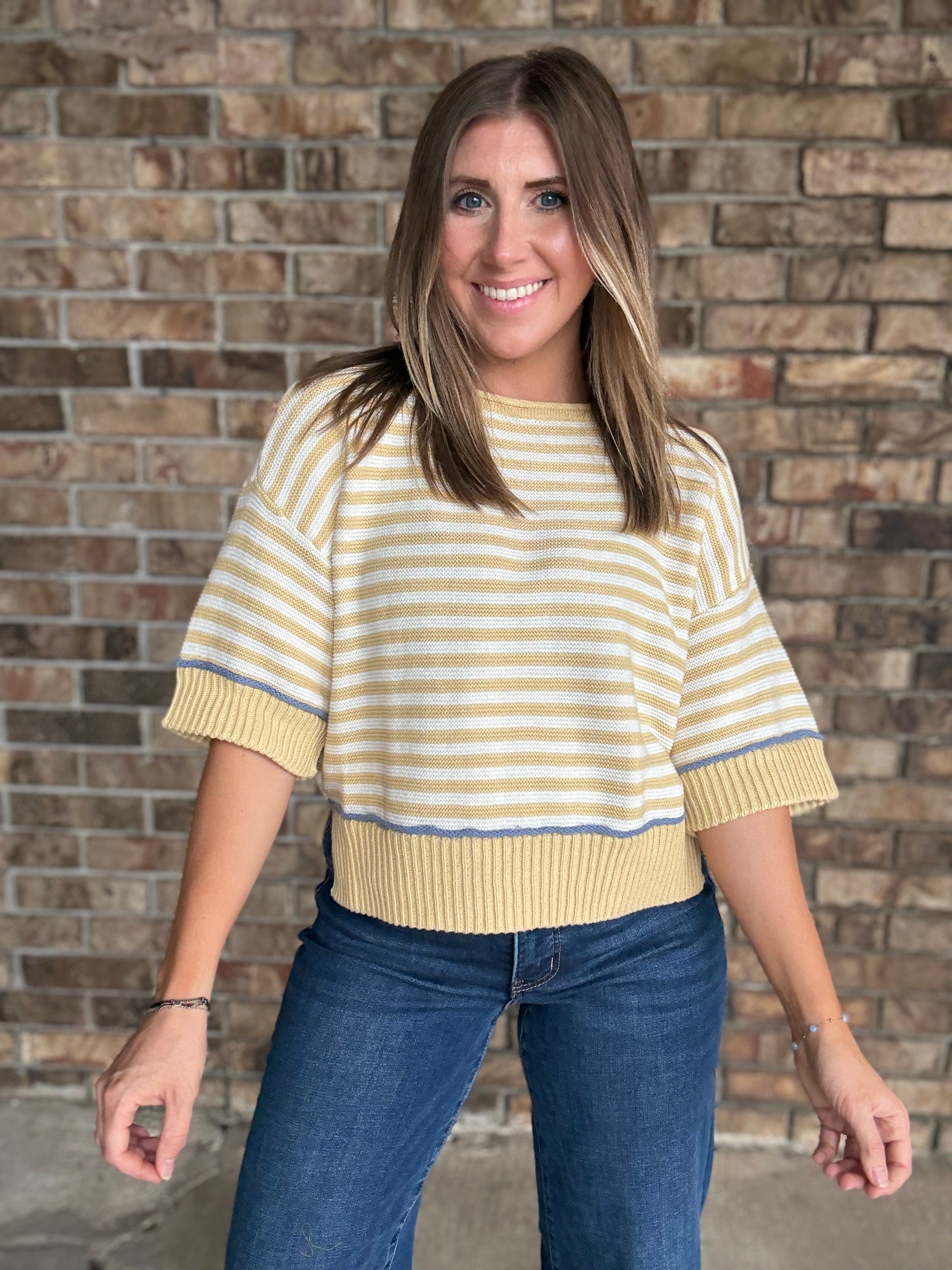 Woman wearing a butter yellow and ivory striped lightweight sweater with raw edge details and dark wash jeans