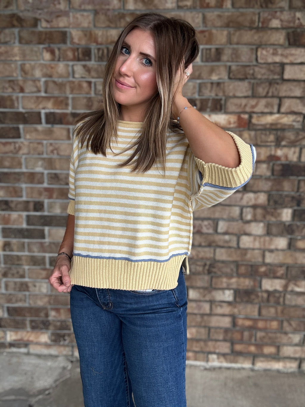 Woman wearing a butter yellow and ivory striped lightweight sweater with raw edge details and dark wash jeans