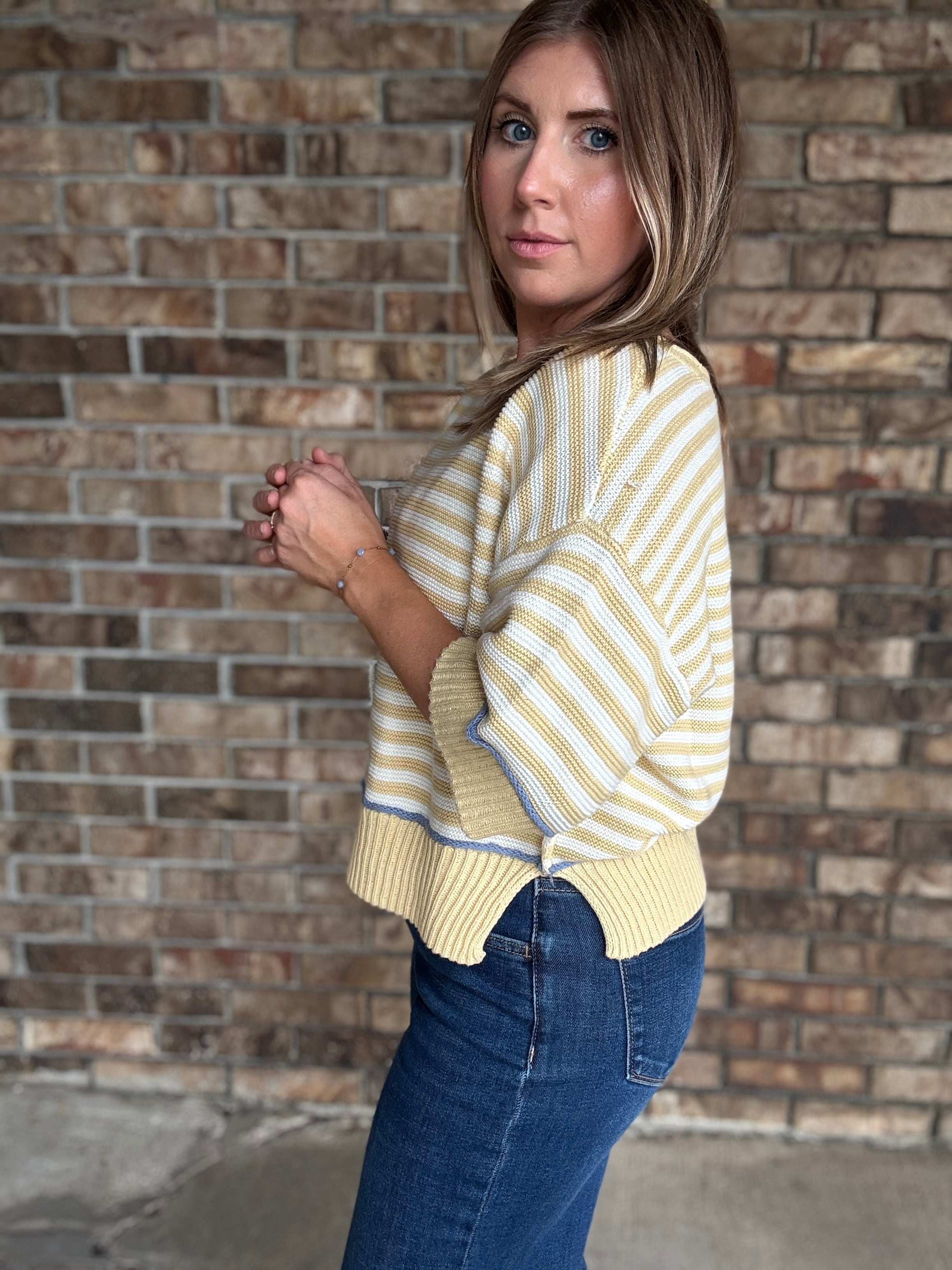 Woman wearing a butter yellow and ivory striped lightweight sweater with raw edge details and dark wash jeans