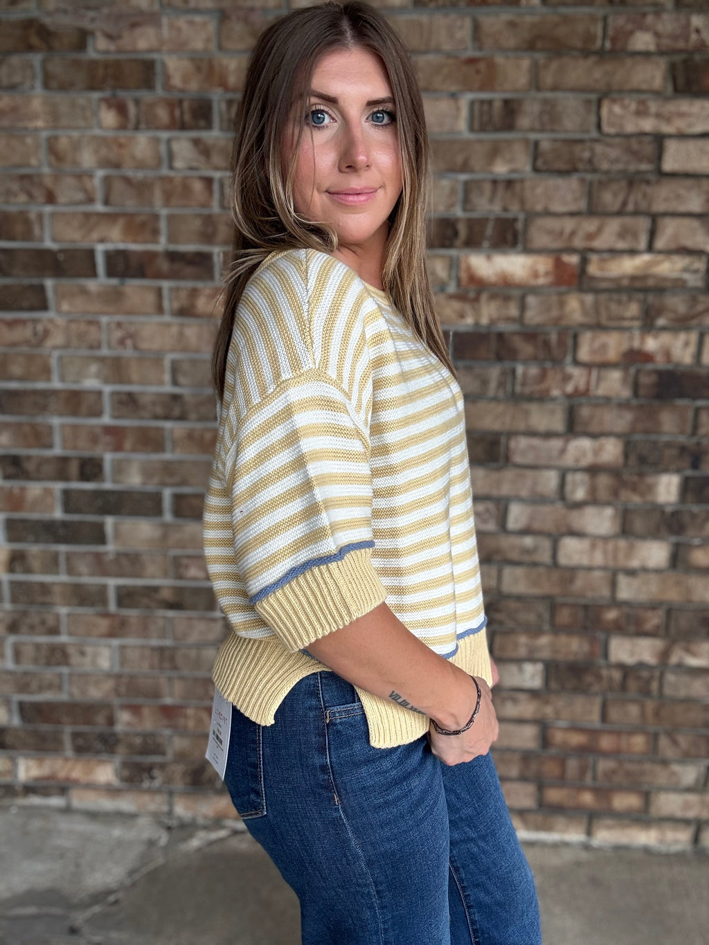Woman wearing a butter yellow and ivory striped lightweight sweater with raw edge details and dark wash jeans