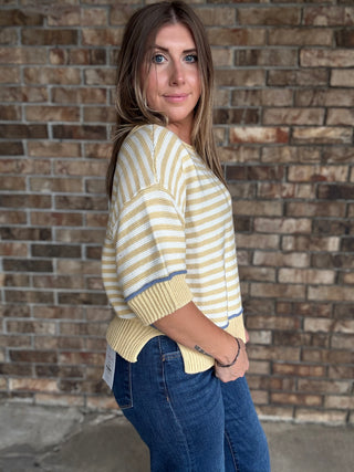 Woman wearing a butter yellow and ivory striped lightweight sweater with raw edge details and dark wash jeans