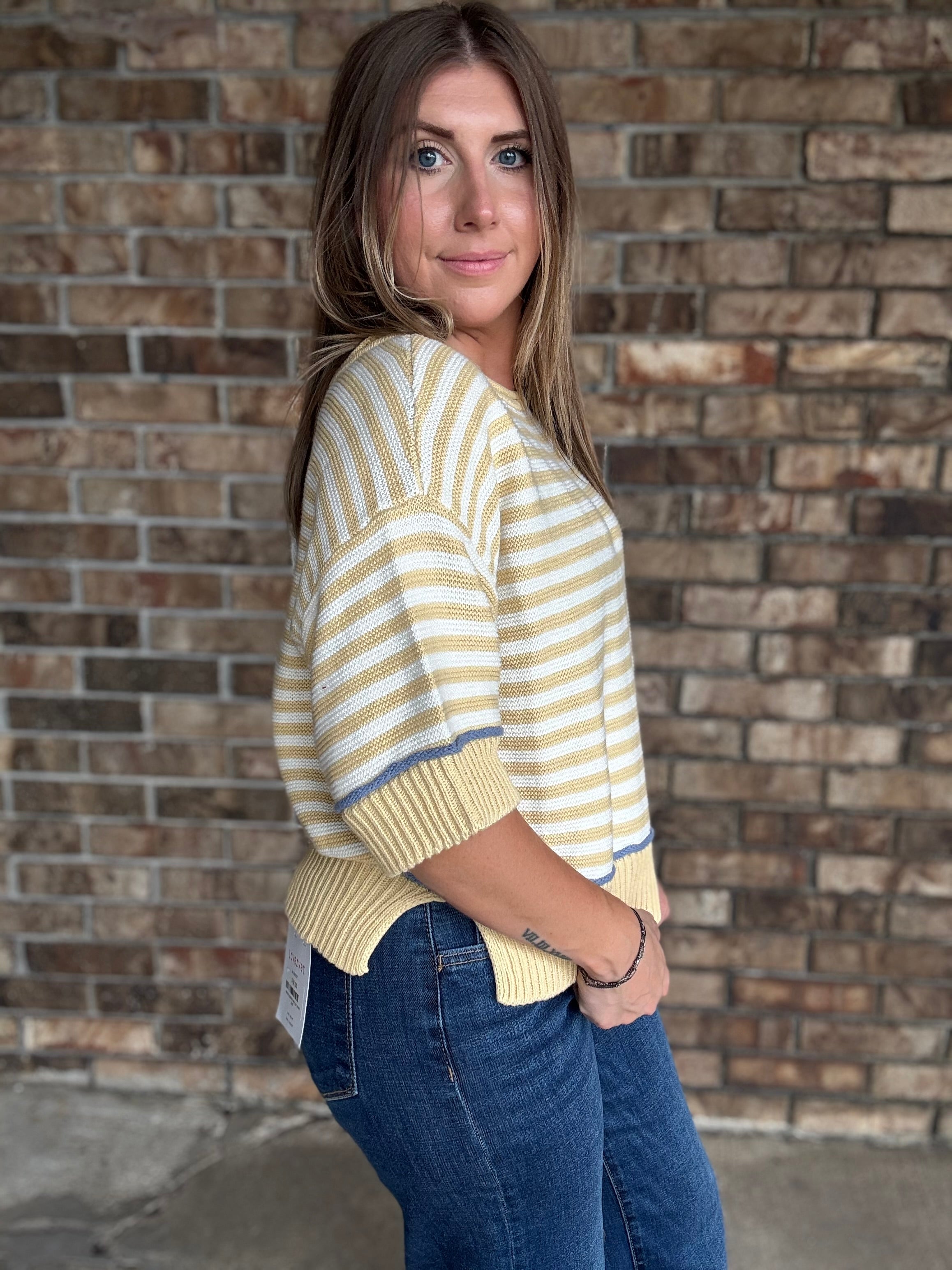 Woman wearing a butter yellow and ivory striped lightweight sweater with raw edge details and dark wash jeans