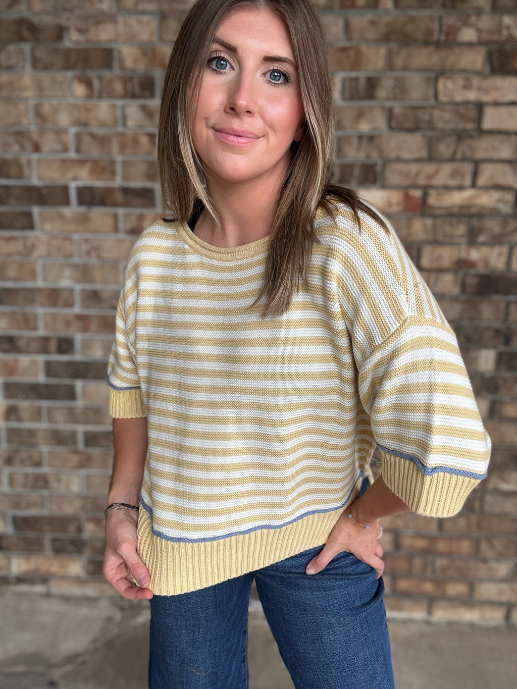 Woman wearing a butter yellow and ivory striped lightweight sweater with raw edge details and dark wash jeans