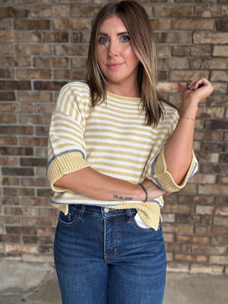 Woman wearing a butter yellow and ivory striped lightweight sweater with raw edge details and dark wash jeans
