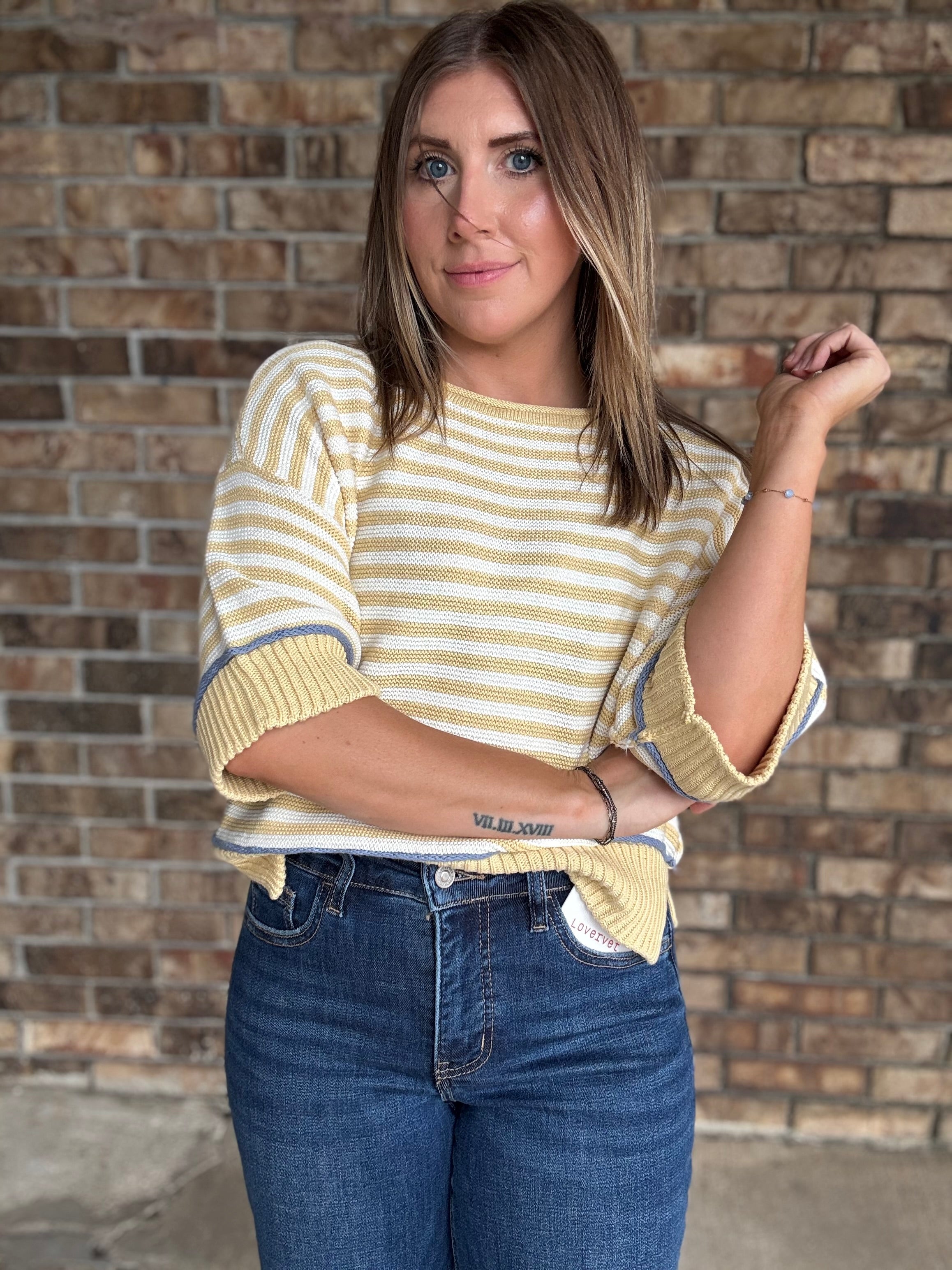 Woman wearing a butter yellow and ivory striped lightweight sweater with raw edge details and dark wash jeans