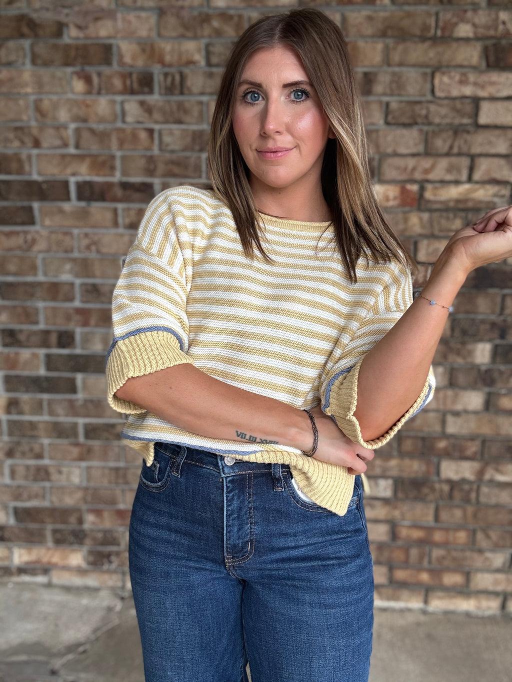 Woman wearing a butter yellow and ivory striped lightweight sweater with raw edge details and dark wash jeans