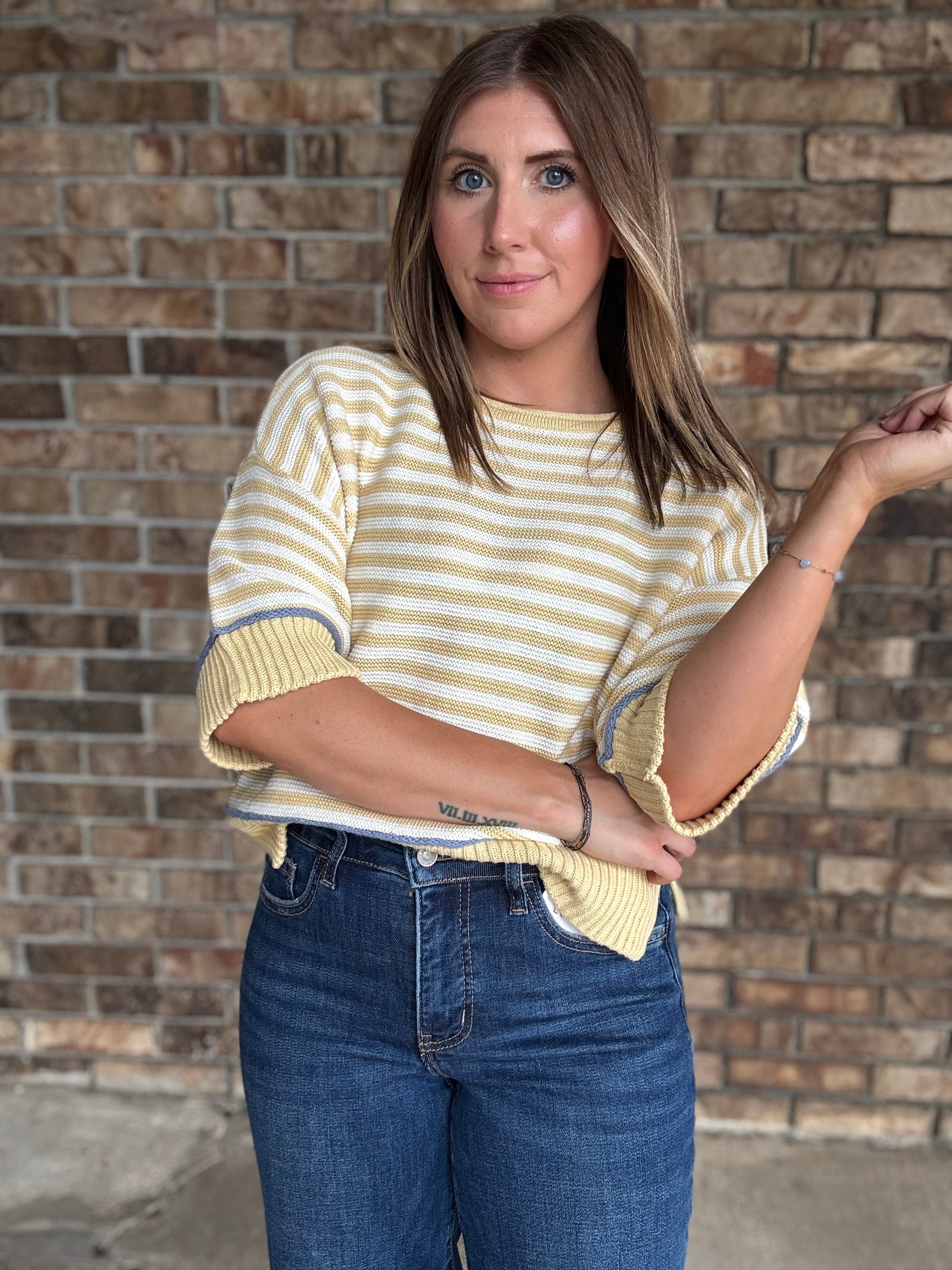 Woman wearing a butter yellow and ivory striped lightweight sweater with raw edge details and dark wash jeans