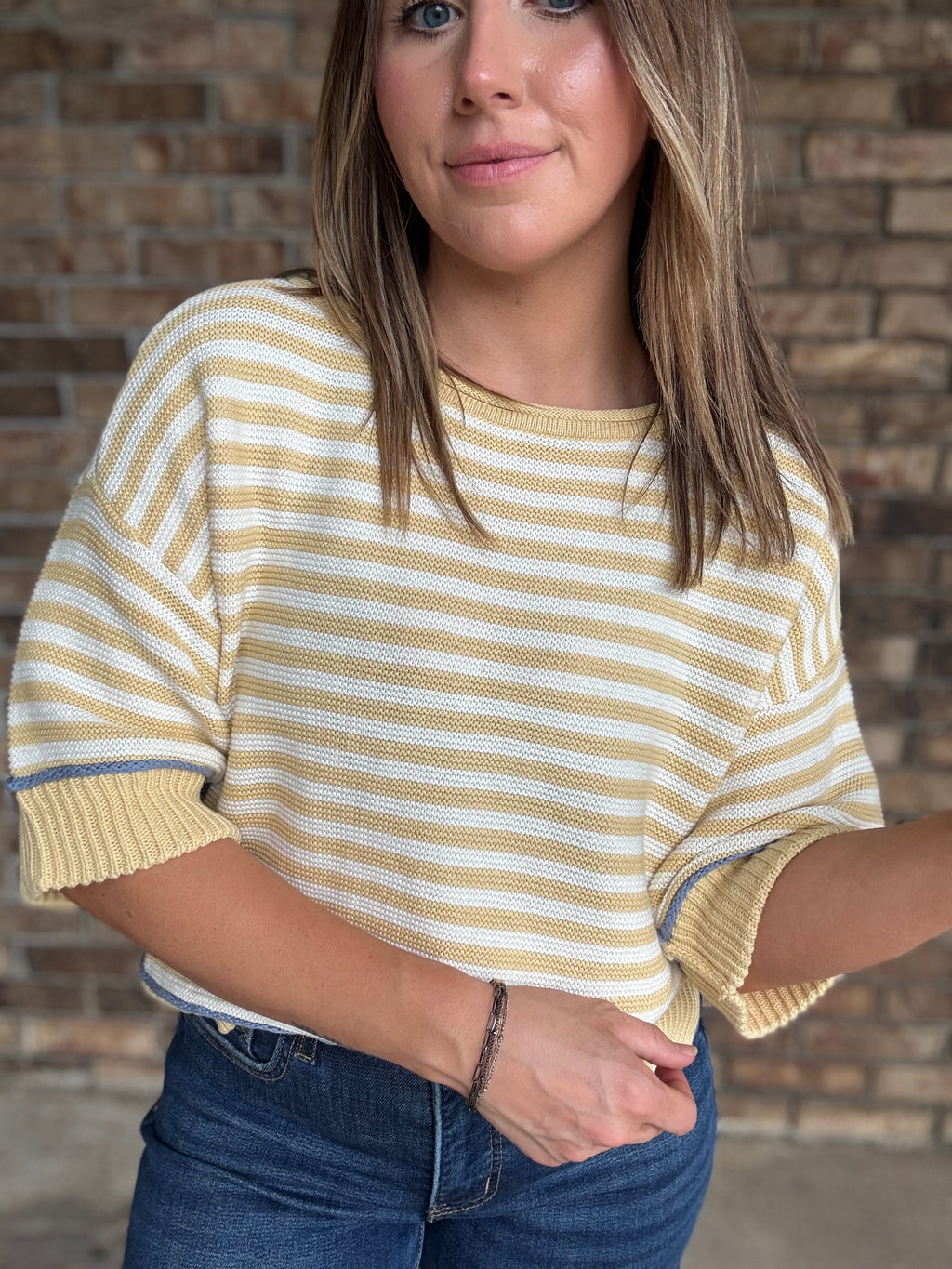 Woman wearing a butter yellow and ivory striped lightweight sweater with raw edge details and dark wash jeans