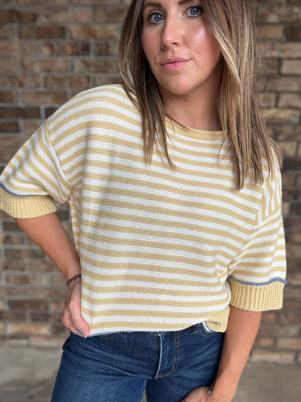 Woman wearing a butter yellow and ivory striped lightweight sweater with raw edge details and dark wash jeans